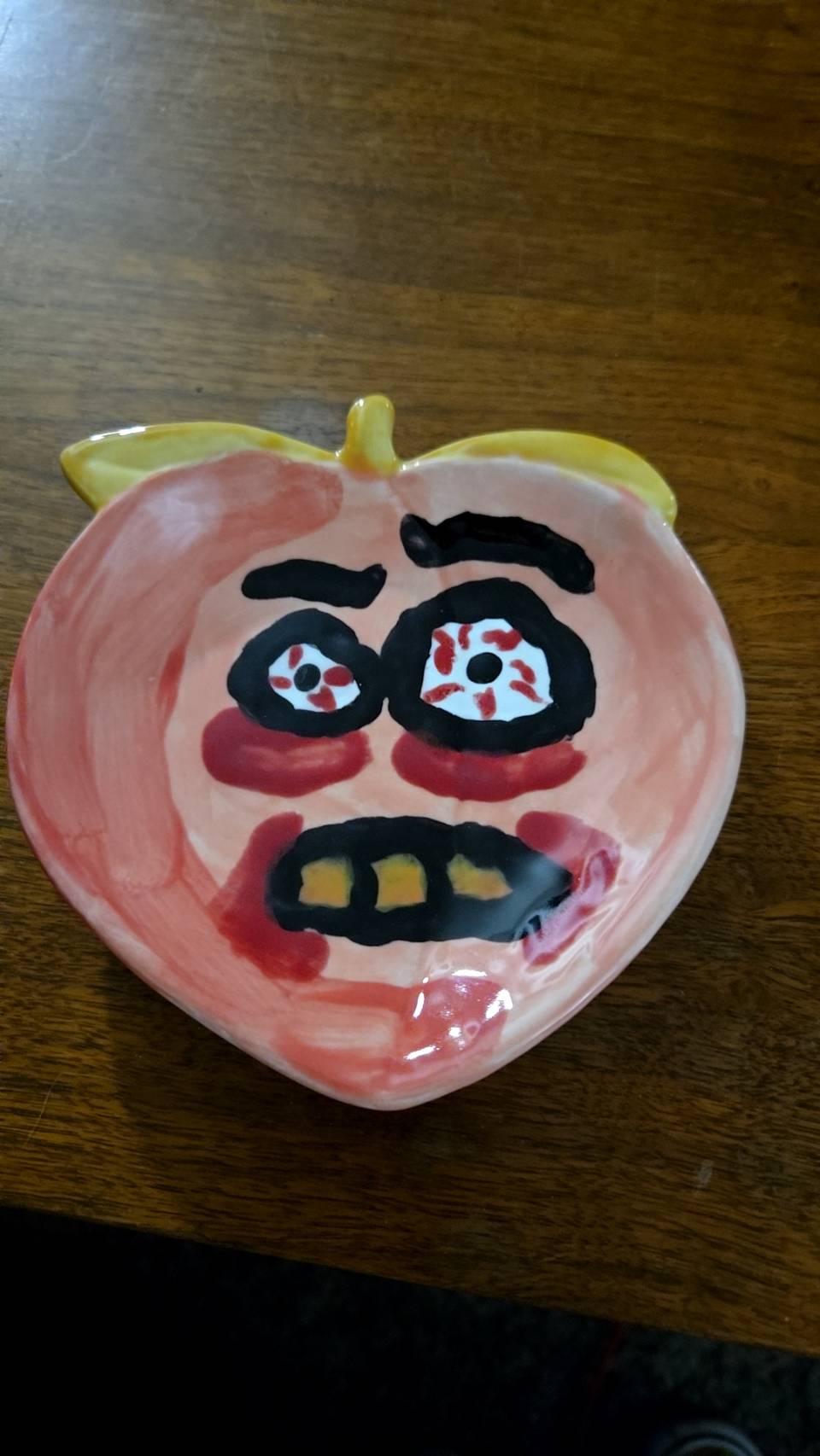 A ceramic tray in the shape of a peach with a distressed facce and yellowed teeth
